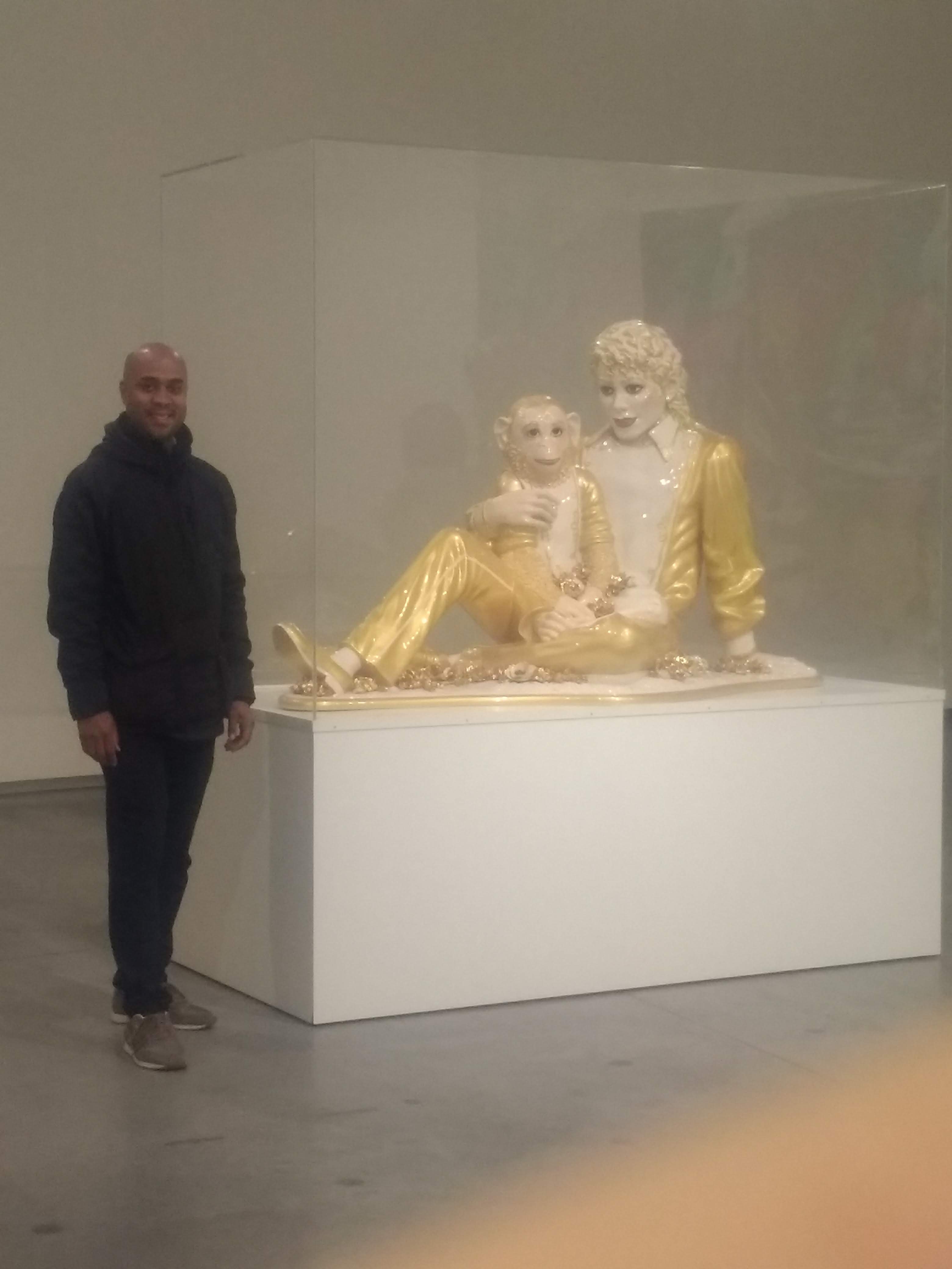 Zak standing next to a piece of art by Jeff Koon's called Michael Jackson and Bubbles is a porcelain sculpture 