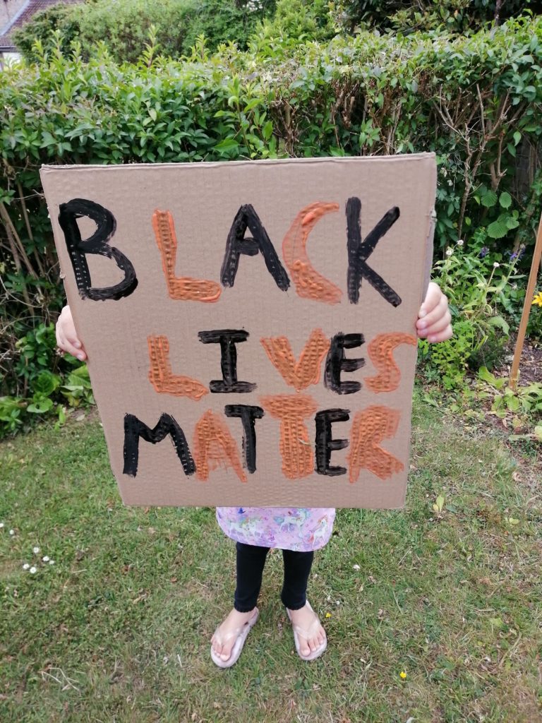 Photo of daughter holding our own sign that reads Black Lives Matter in orange and black.