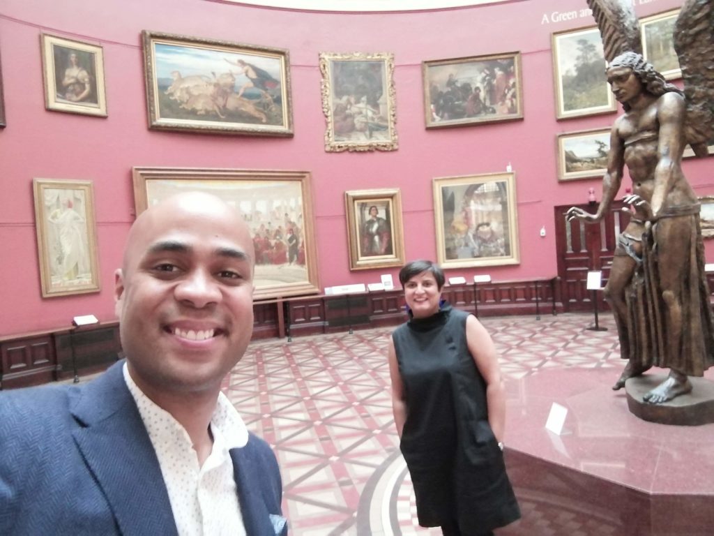 Photo of Sara and Zak standing in the main hall at Birmingham Museum & Art Gallery with paintings in the background